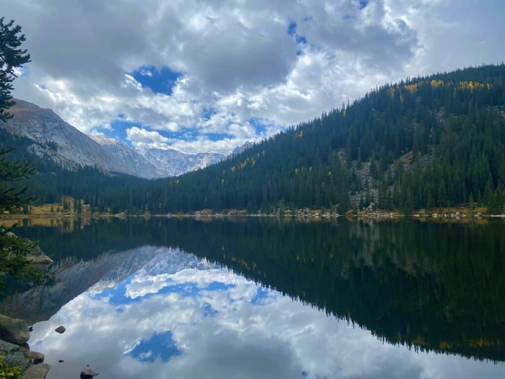 reflective blue lake with blue jagged rocky mountains behind 