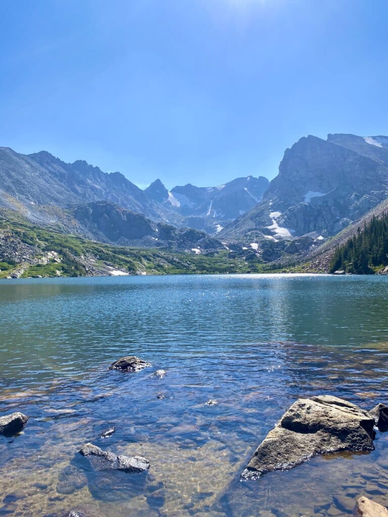 rocky mountains with snow on them and a turquoise blue lake with rocks 