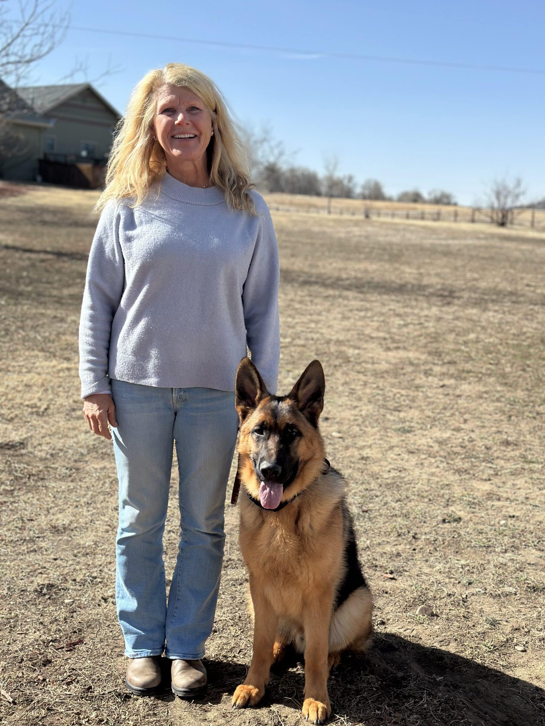 german shepherd standing next to a middle aged blond lady with jeans and grey shirt on